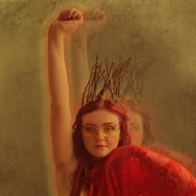 megan wears a red shawl and raises her right arm in the air with a fist
