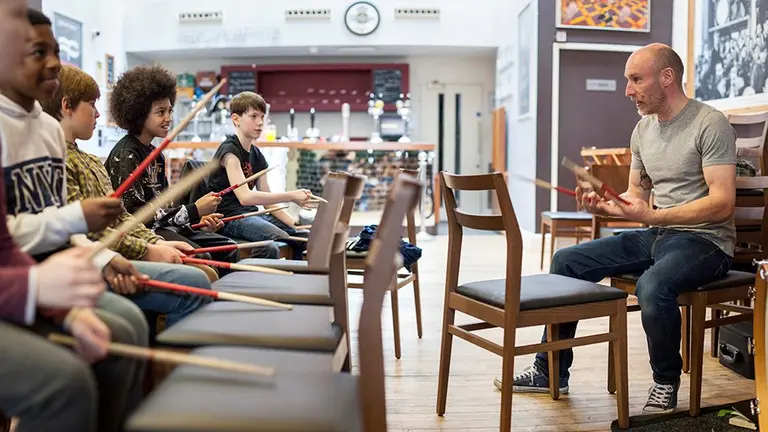 Music teacher teaching kids to drum using sticks and chairs