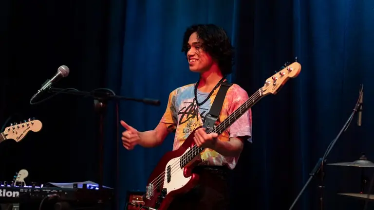 Young man on stage with guitar smiling and giving thumbs up sign