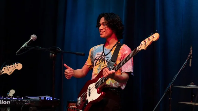 Young man on stage with guitar smiling and giving thumbs up sign