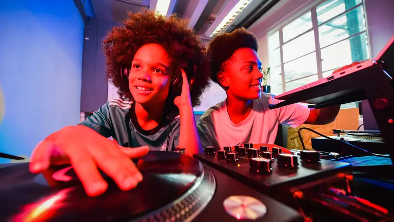 two young boys on a dj deck, faces lit up in orange