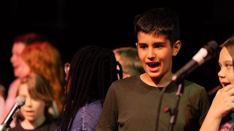 young adults singing on a dark stage, two microphones in front of them