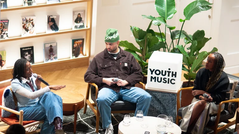 Youth Music and Levi's panel event. 4 young people sat in a semi circle around a Youth Music sign, plants in background, with a shelf of magazines behind.