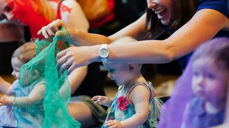 Woman smiling playing with green material with happy baby in a group project
