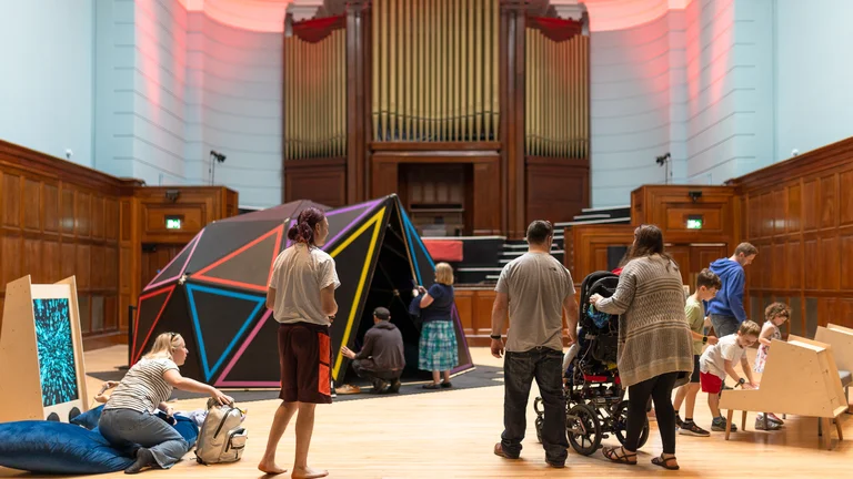 Image of Soundplay's immersive experience, with an organ at the end of a large room, and children playing in their sensory dome.