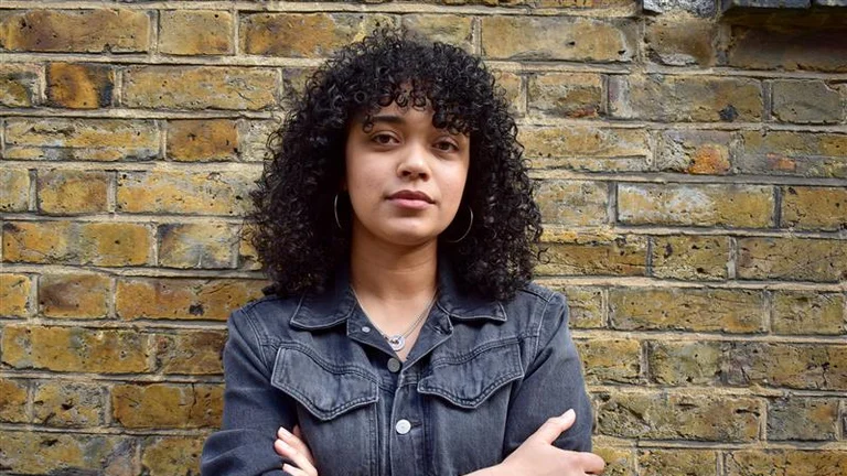 Image of Insights Manager, Remi Fairweather Stride, standing in front of a brick wall with arms folded.