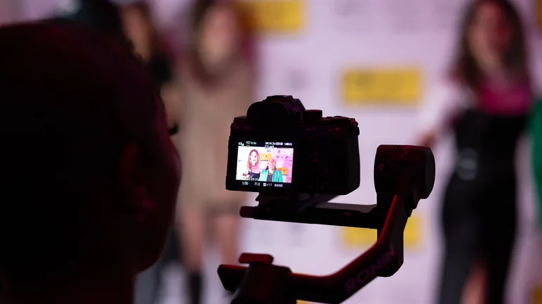 a camera photographs people on a red carpet
