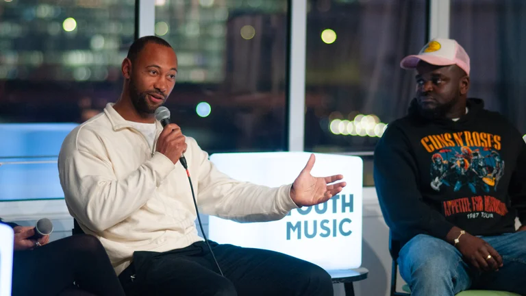 a man wearing holds a microphone and speaks on a panel