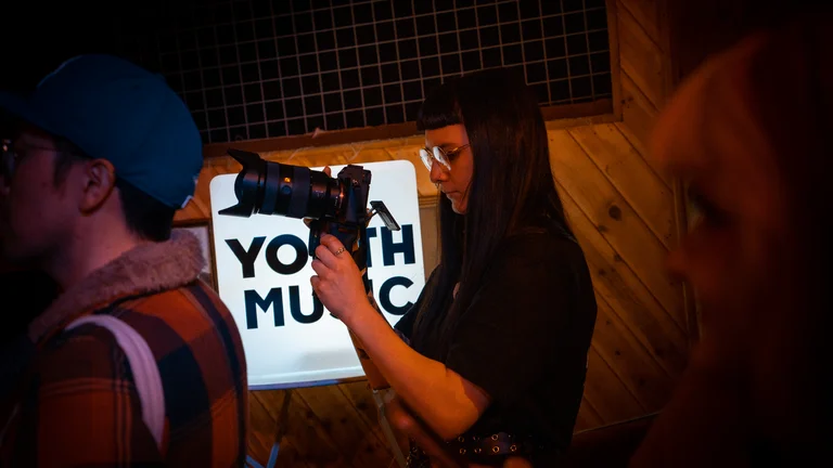 a girl with dark straight hair and glasses holds a professional camera