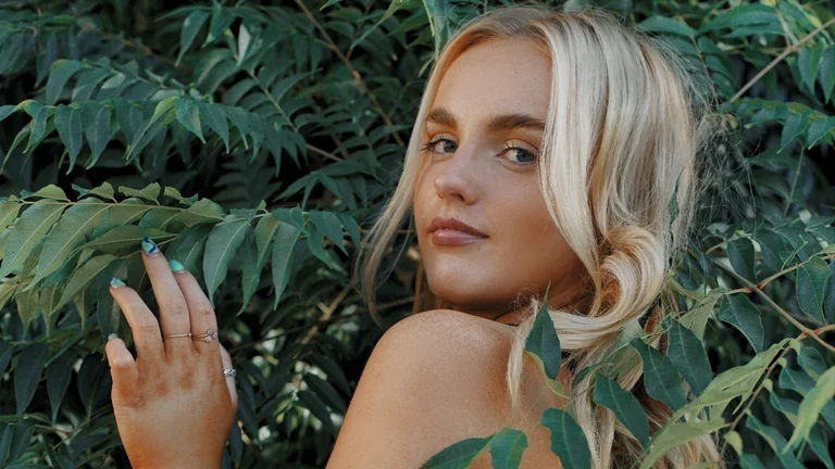 matilda poses amongst green leaves. she has light blonde hair and looks over her shoulder