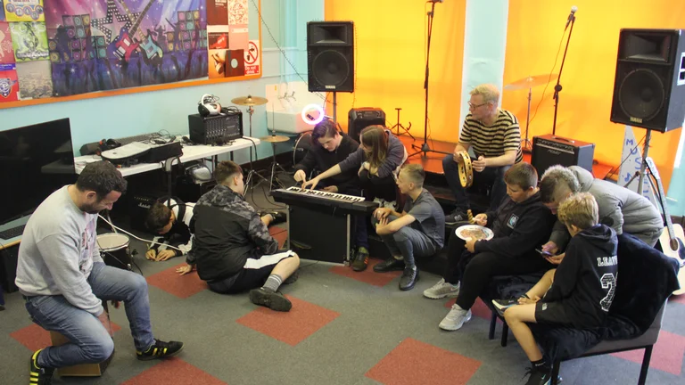 Image of a My Pockets music sessions. Young people huddled around instruments 