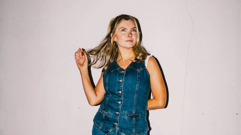 jodie bryant wears a sleeveless button up denim dress. she plays with her blonde hair