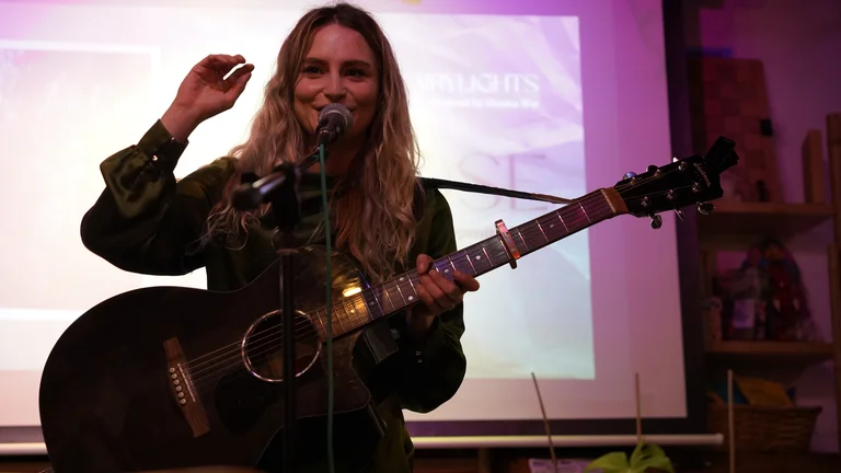 cat rose holds an acoustic guitar and stands in front of a mic on stage