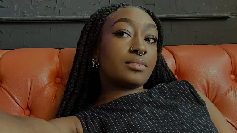 a woman with braids and a septum piercing reclines on a leather sofa and takes a selfie