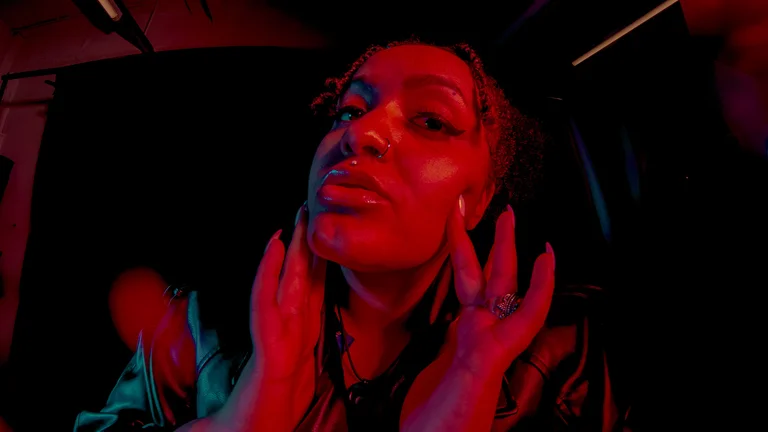 a woman holds her hands up to her face and leans into the camera under red studio lighting