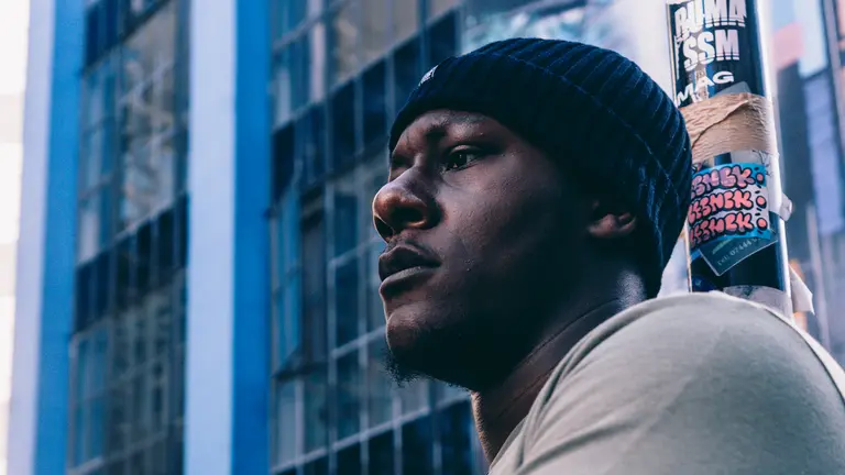 amadeus wears a black beanie and poses against a cityscape