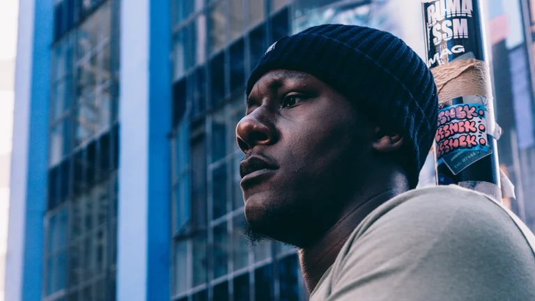amadeus wears a black beanie and poses against a cityscape