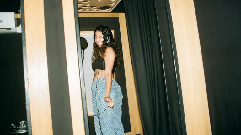 hana smiles in the recording studio, wearing a black crop top and blue jeans