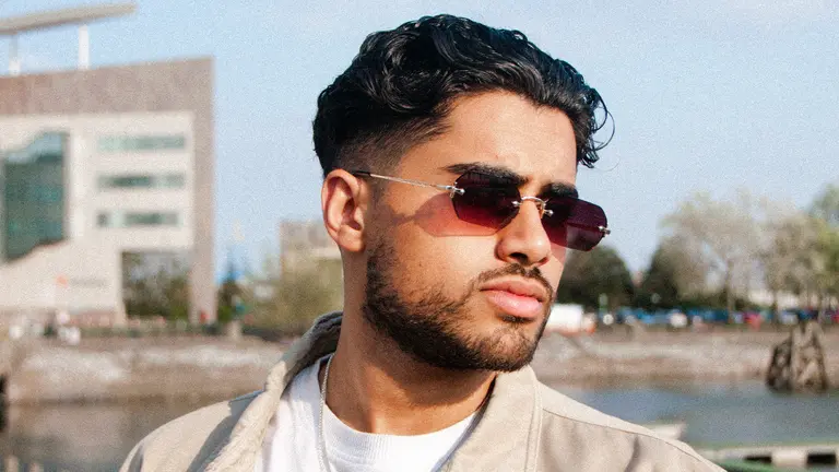 a south asian man with slicked back dark wavy hair wears tinted subglasses