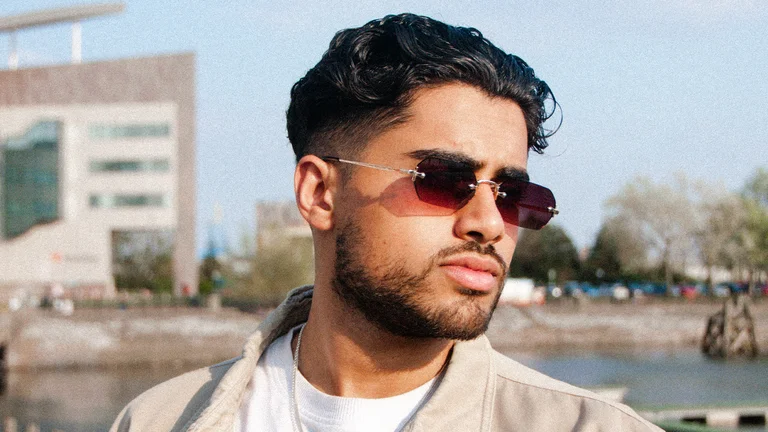 a south asian man with slicked back dark wavy hair wears tinted subglasses