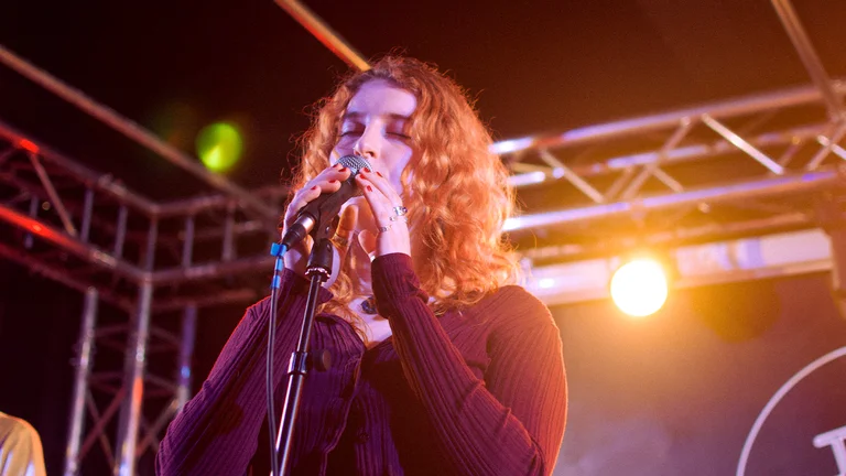 a woman with curly auburn hairs sings into a mic on stage