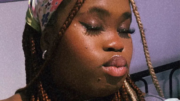 a woman with braids and a headscarf pouts with her eyes closed