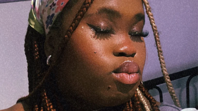 a woman with braids and a headscarf pouts with her eyes closed