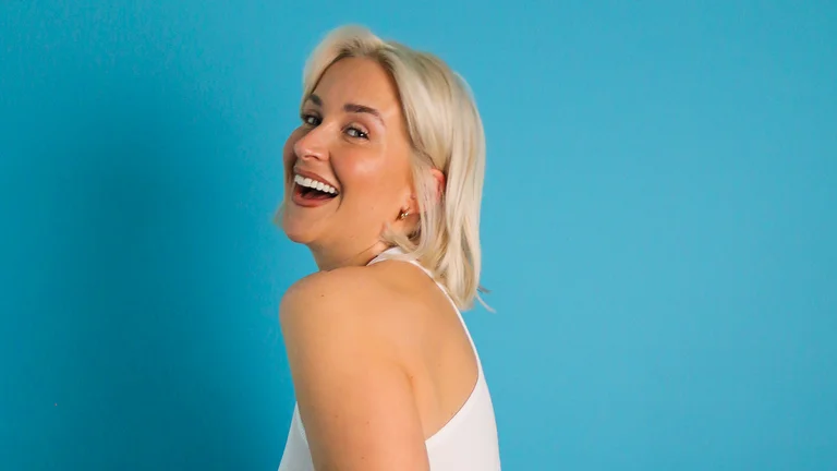kennedy taylor hair a blonde bob. she poses against a blue backdrop and laughs