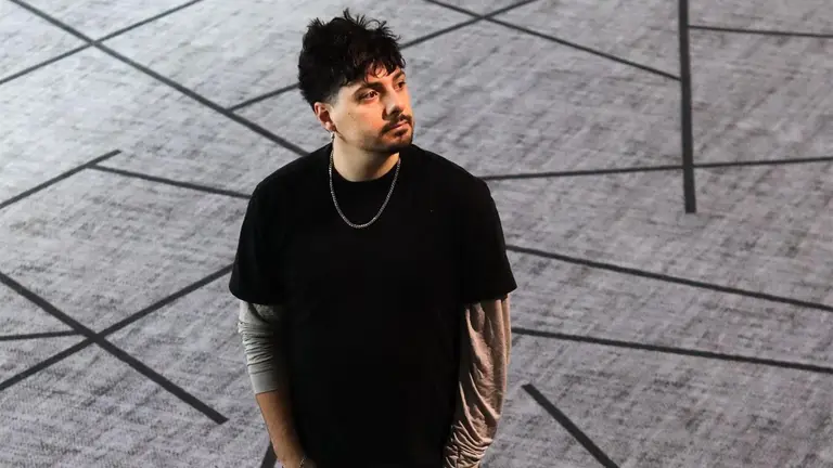 numa has short dark hair and a moustache. he wear a black t shirt wiht a silver chain