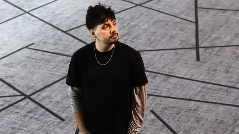 numa has short dark hair and a moustache. he wear a black t shirt wiht a silver chain