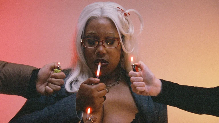 a woman with bleach blonde hair holds up a lighter to light a cigarette, two other hands also hold up lighters 