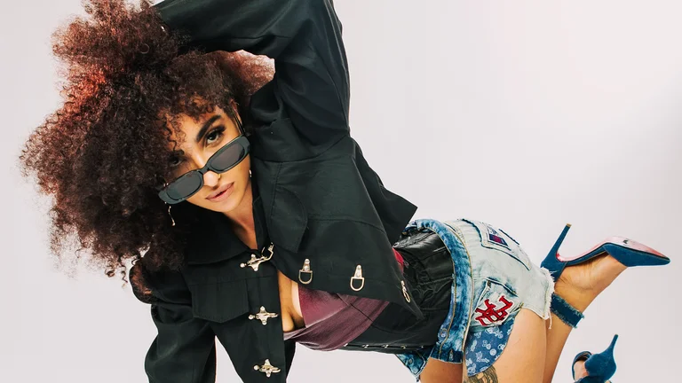 roukaya poses in a fashionable outfit, her hand in her curly hair