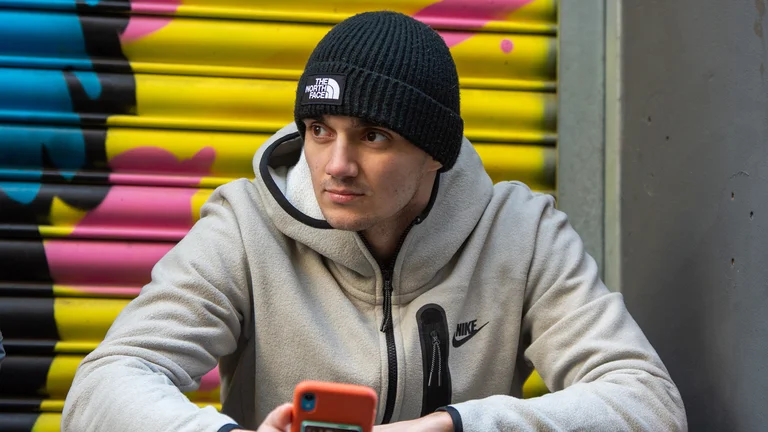 ryrhyme wears a north face beanie and nike grey zip ip hoodie. he sits on the floor and holds a phone