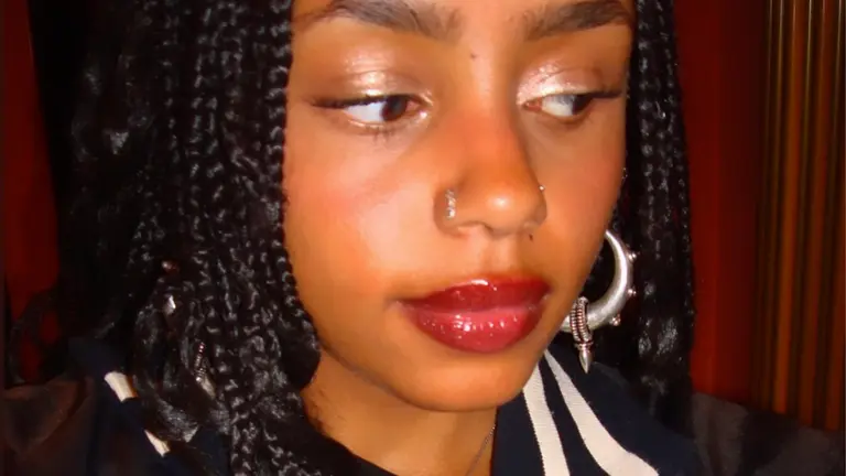 theadora has a silver nose ring and black braids. she has rouge lip gloss and shimmery eyeshadow