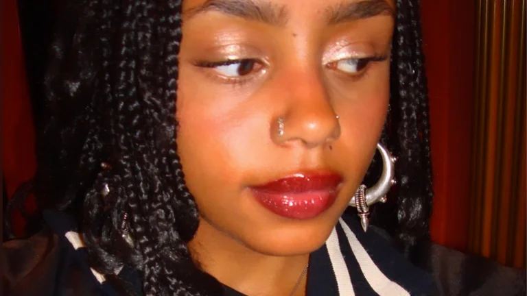 theadora has a silver nose ring and black braids. she has rouge lip gloss and shimmery eyeshadow