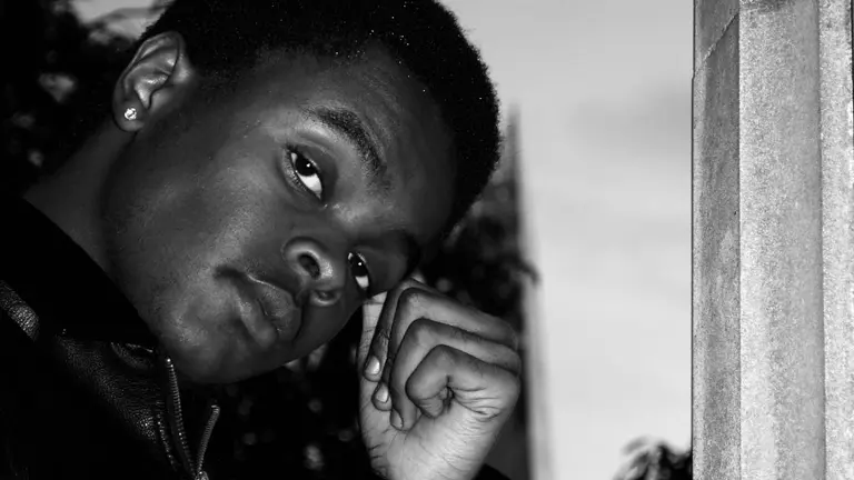 Image of Kasim, black and white, hand to his head, looking at the camera
