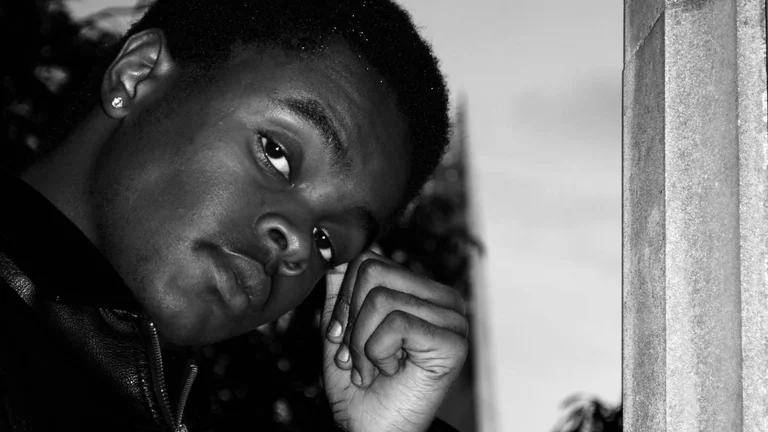 Image of Kasim, black and white, hand to his head, looking at the camera