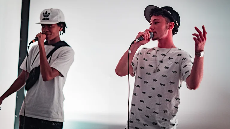 two young men in caps perform with mics