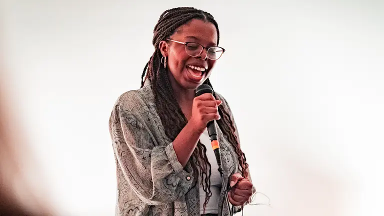 a woman with braids and glasses sings into a mic