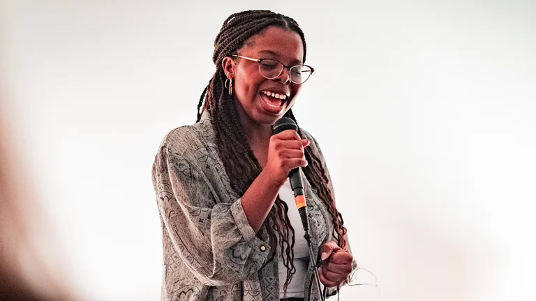 a woman with braids and glasses sings into a mic
