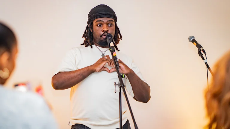 a man in a white tshirt and beanie sings into a mic