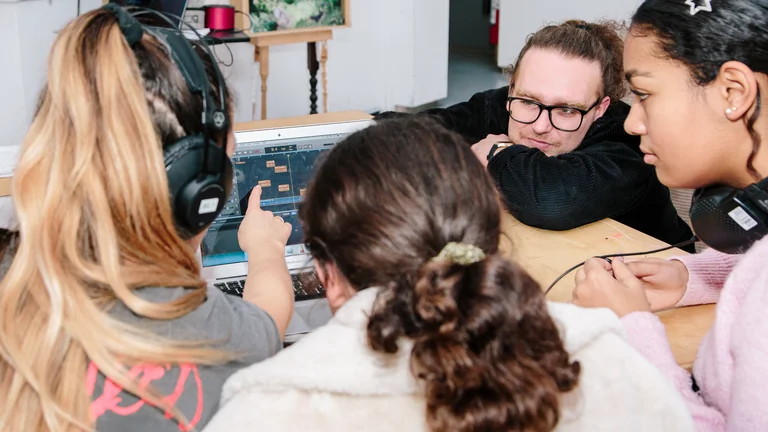 young people crowding around a laptop with music software with their teacher