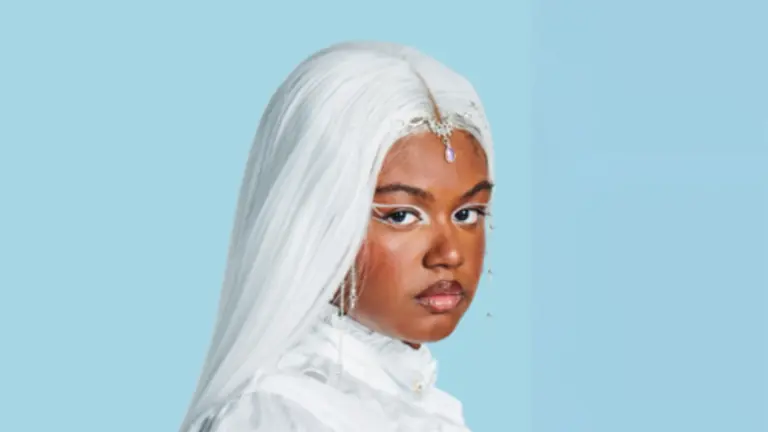 Nyrobi dressed in white, with white hair, looking over her shoulder at the camera