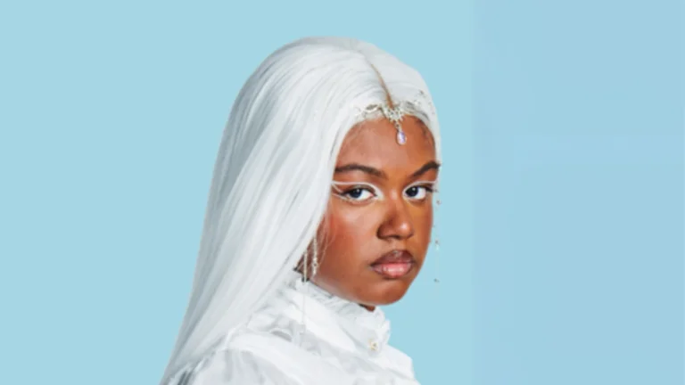 Nyrobi dressed in white, with white hair, looking over her shoulder at the camera