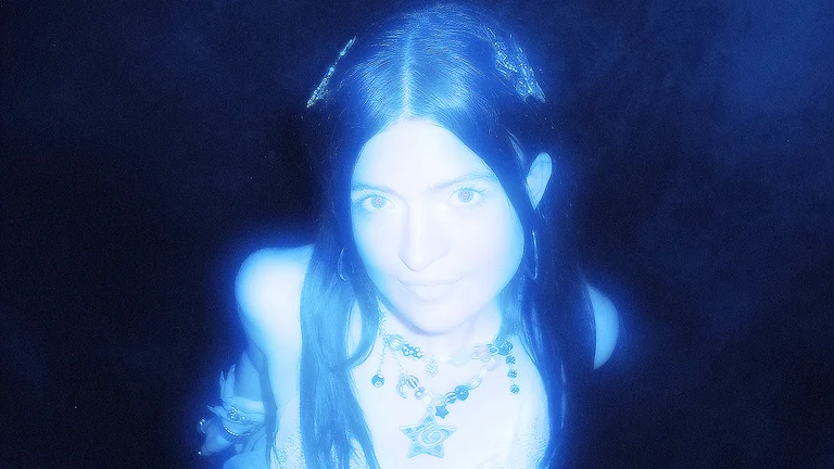 melba is illuminated in an ethereal blue light; she looks at the camera
