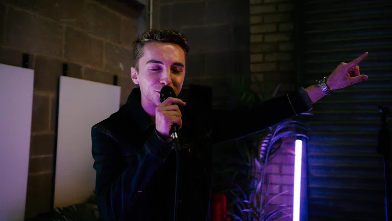 a young man sings into a microphone and raises his left arm