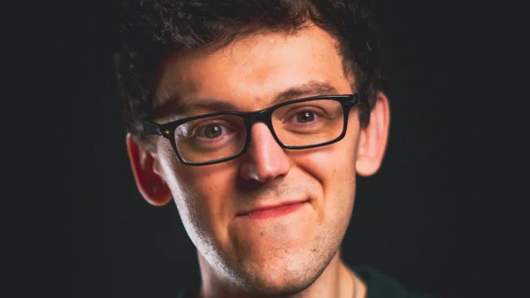 Charlie Baxter headshot, wearing black glasses in front of a black background