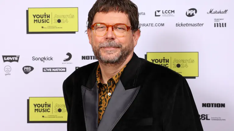 Matt Griffiths at the Youth Music Awards, wearing a black suit with grey lapels, a tiger print shirt, and red-rimmed glasses