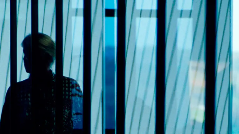 A person stands in the blue background. We can only see the silhouette against a window. 