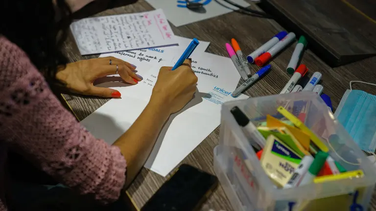 A person with a pink jumper writing in a paper with blue ink